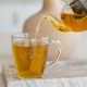 Een theeglas met daarop het Lottea logo. Het theeglas wordt ingeschonken met thee uit een theepot.