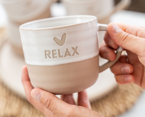 Lottea-Theemok-Relax Een theemok met daarop relax. De bovenkant is wit en de onderkant steen oranje en de theemok heeft een oor.