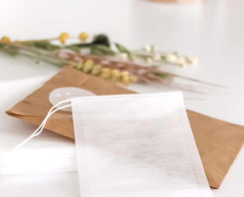Witte biologisch afbreekbare theefilter zakje op een bruine verpakking met daarachter nog een klein bosje droogbloemen.