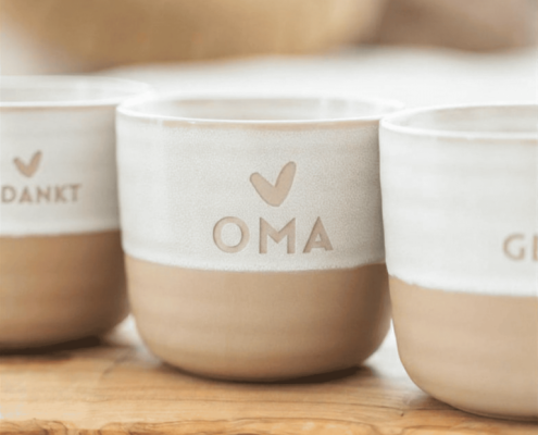 Een theemok met oma en een hartje erop. De bovenkant van de mok is wit, de onderkant steenbruin.